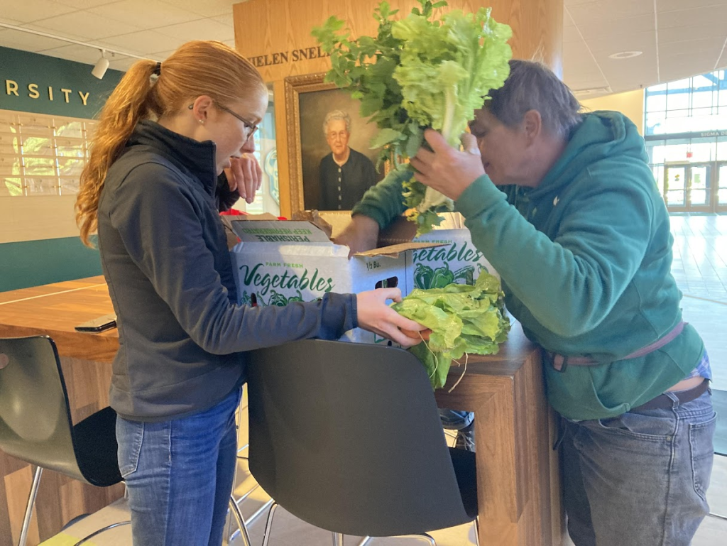Student Ella Weldy and Farmer Dulli Tengeler go through a student CSA box on a table in the Cheel Arena atrium. Dulli is pulling lettuce and lemon balm from the box.