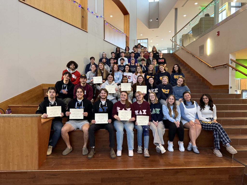 A group of fraternity and sorority students holding their award certificates are sitting in the Student Center Forum after their awards ceremony.