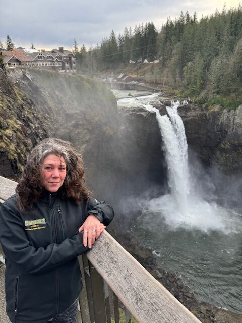 Portrait of Katie Kavanagh with a large waterfall in front of a large hotel in the background.
