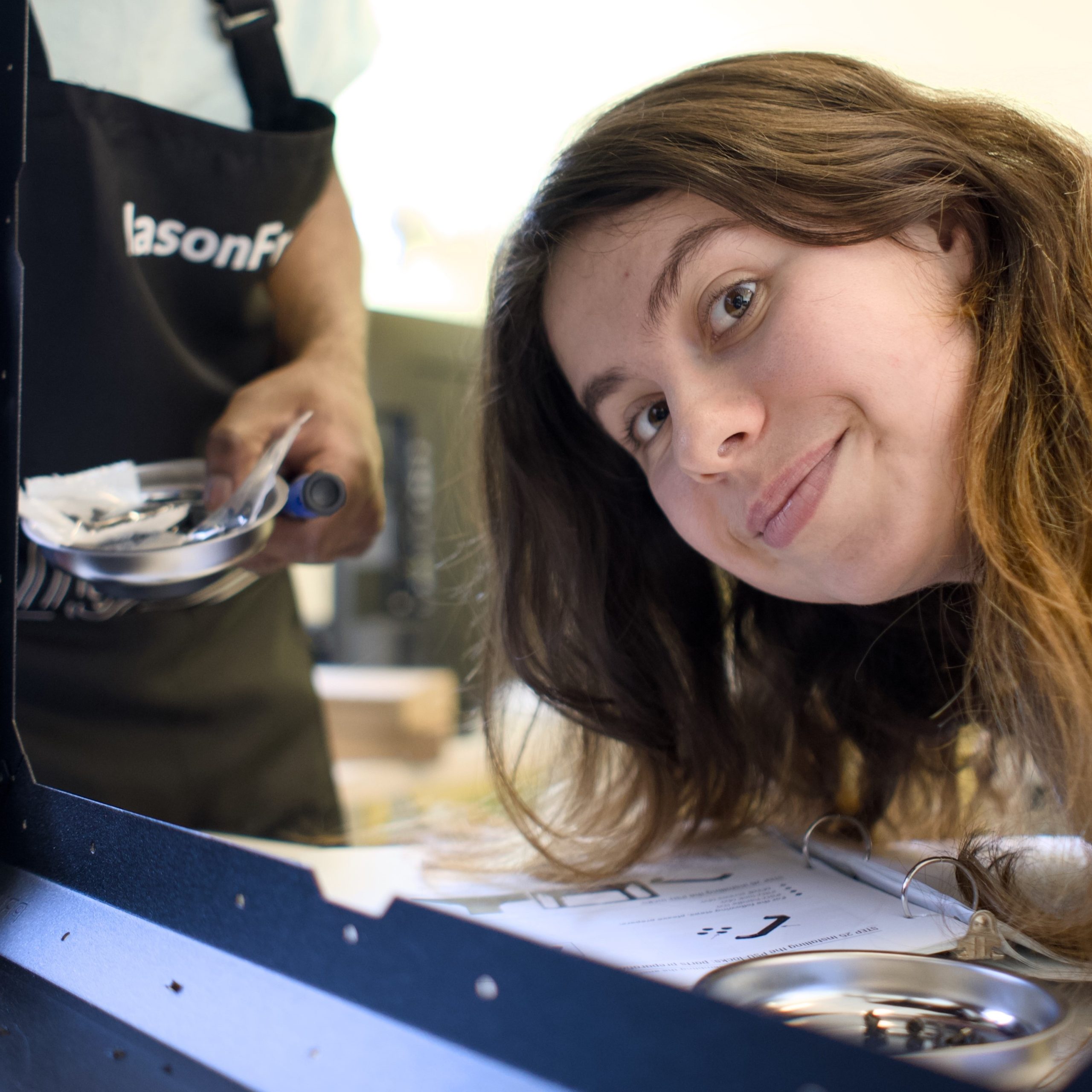 A Maker Mentor smiles into the camera while assembling a metal enclosure.