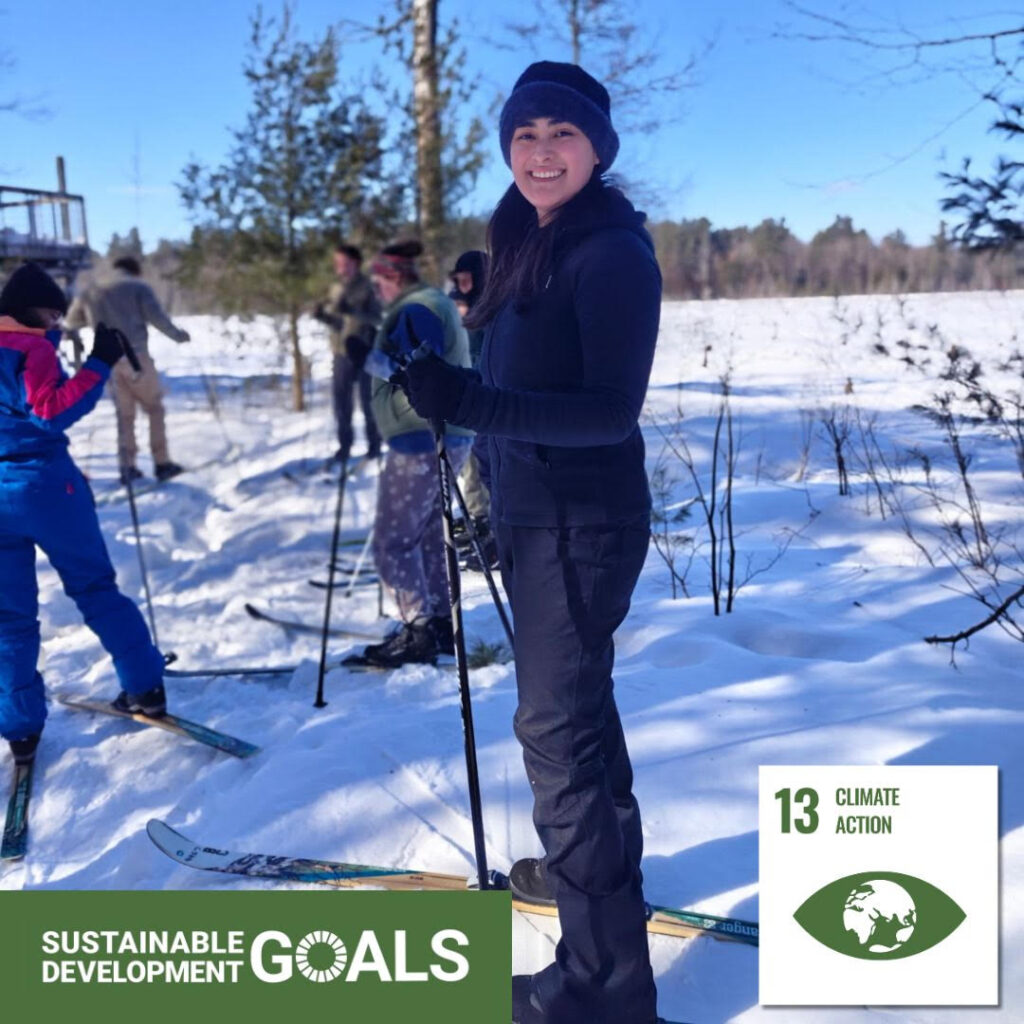 A young woman wearing a winter hat on cross country skis standing in the snow. Text on the image reads "sustainable development goals, thirteen, climate action."