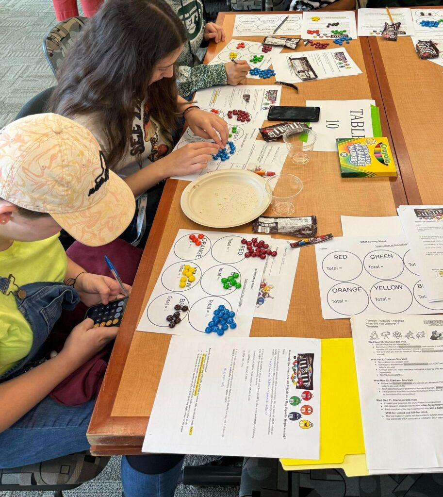 Middle school students sit at a table grouping M&Ms by color for a statistics exercise.