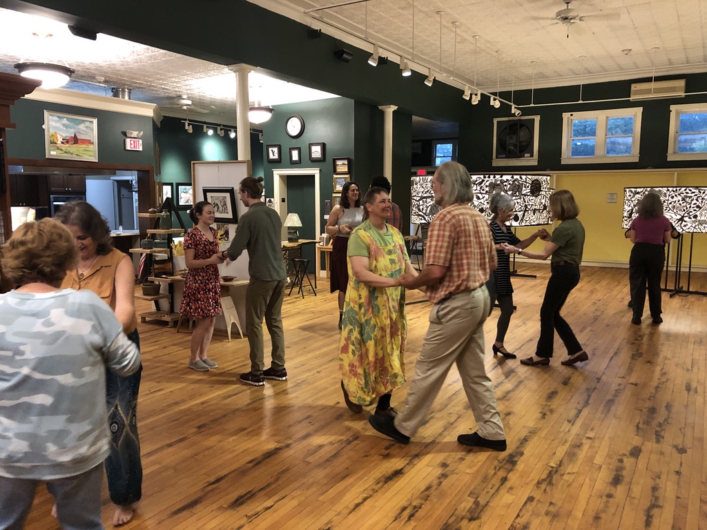 Several pairs of dance partners spread across the hardwood floor of an art gallery work on salsa dance moves. 