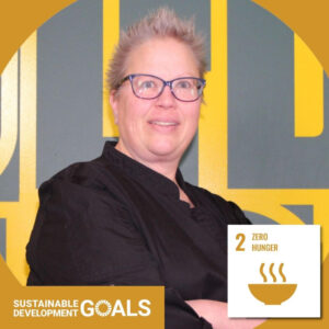 A woman in a chef's shirt with short hair and purple glasses. Text reads "Sustainable Development Goals" and "Zero Hunger."