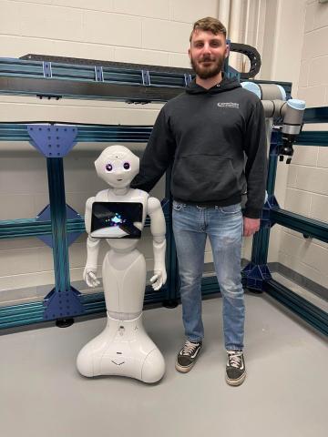 a student stands posed with a robot