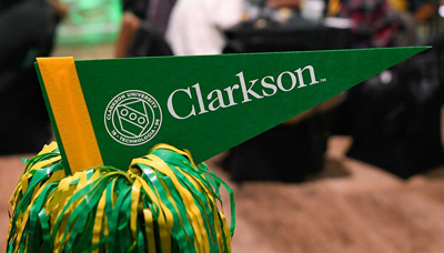 A green pennant with Clarkson University's logo is displayed nestled into a green and yellow pom-pom