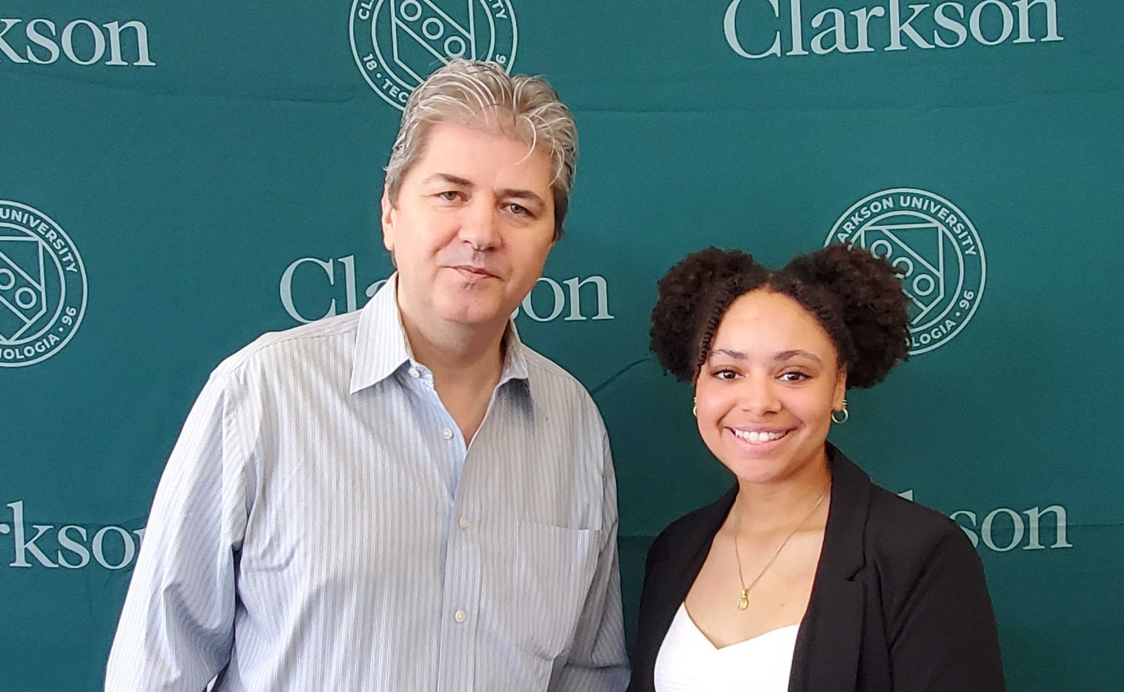 Costel Darie and Kaya Johnson posing for a photo in front of a Clarkson University media backdrop