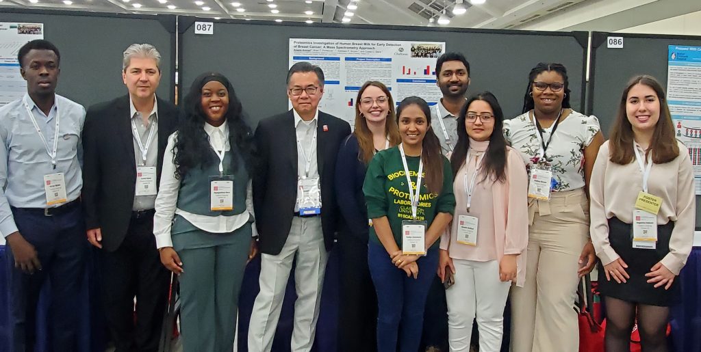 Several students stand with professors in front of a poster presentation setup
