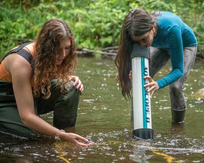 photo of two female students standing in river collecting data