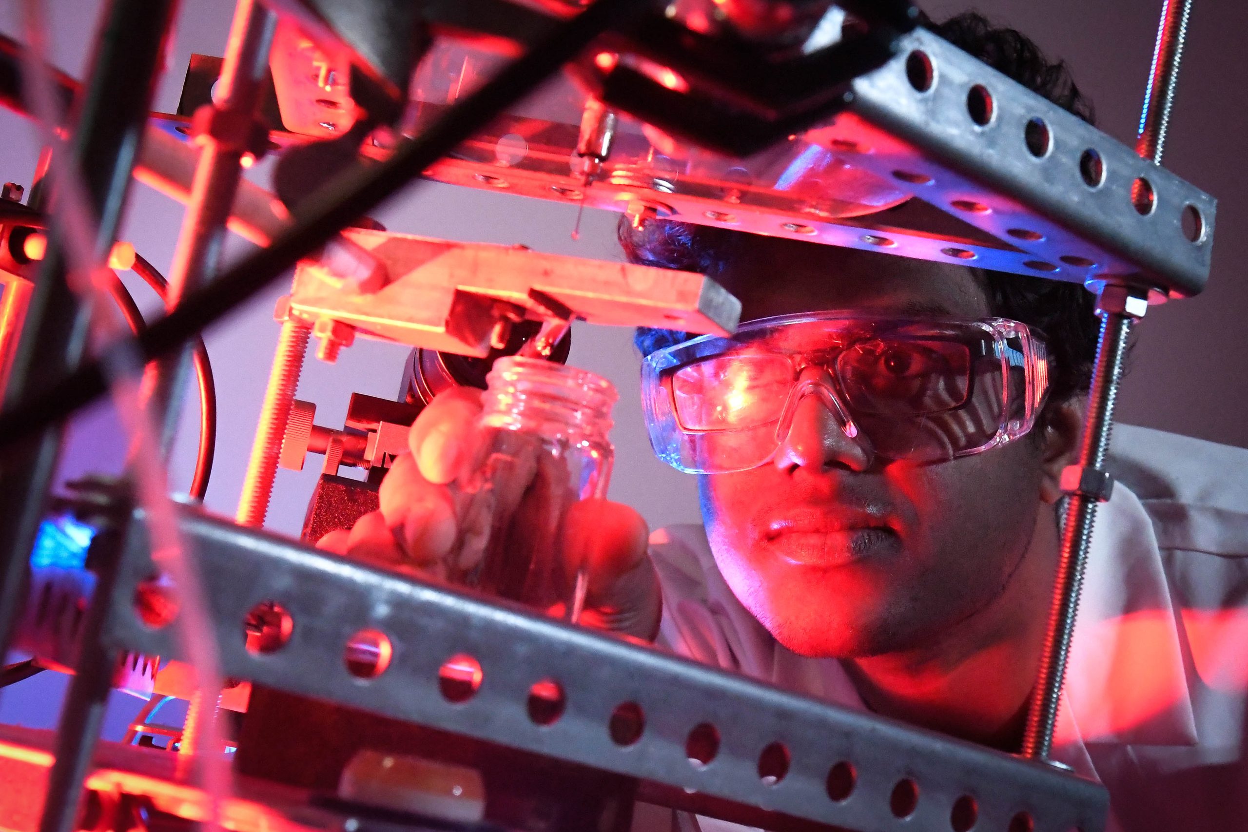 a student in a lab coat and glasses uses lab equipment under red lighting