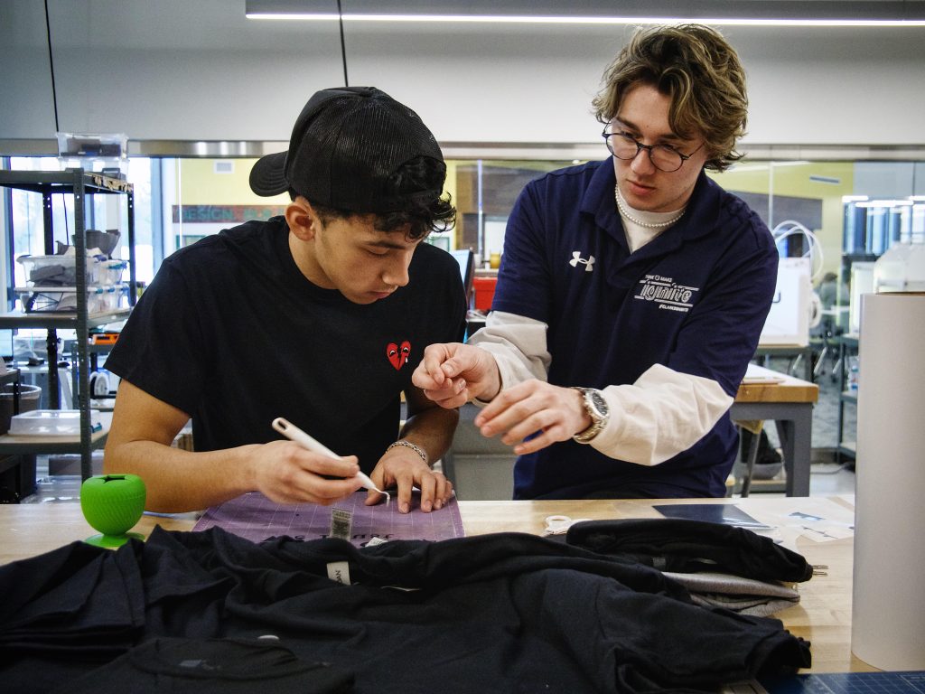 Makerspace Maker Mentor assisting a student with trimming excess vinyl from a cut design.