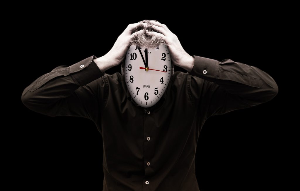 Man with a clock for a face, holding his head with both hands on the top of his head.