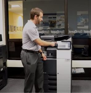 Trainer standing in front of printer, pointing to touch screen 