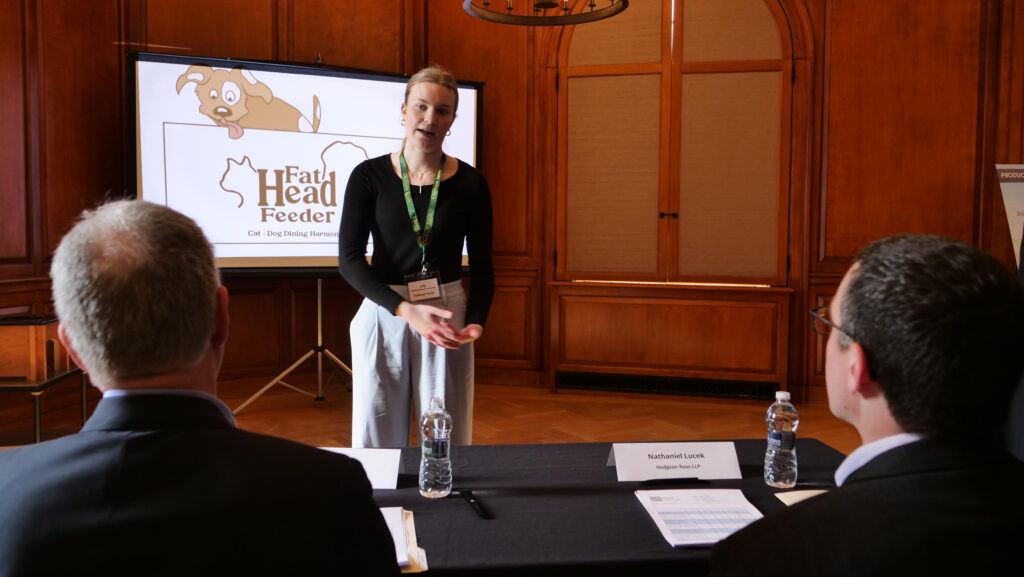 The image features a student from one of the Cube Teams, Fat Head Feeders, pitching her business at the North Country Regional Business Plan Competition.