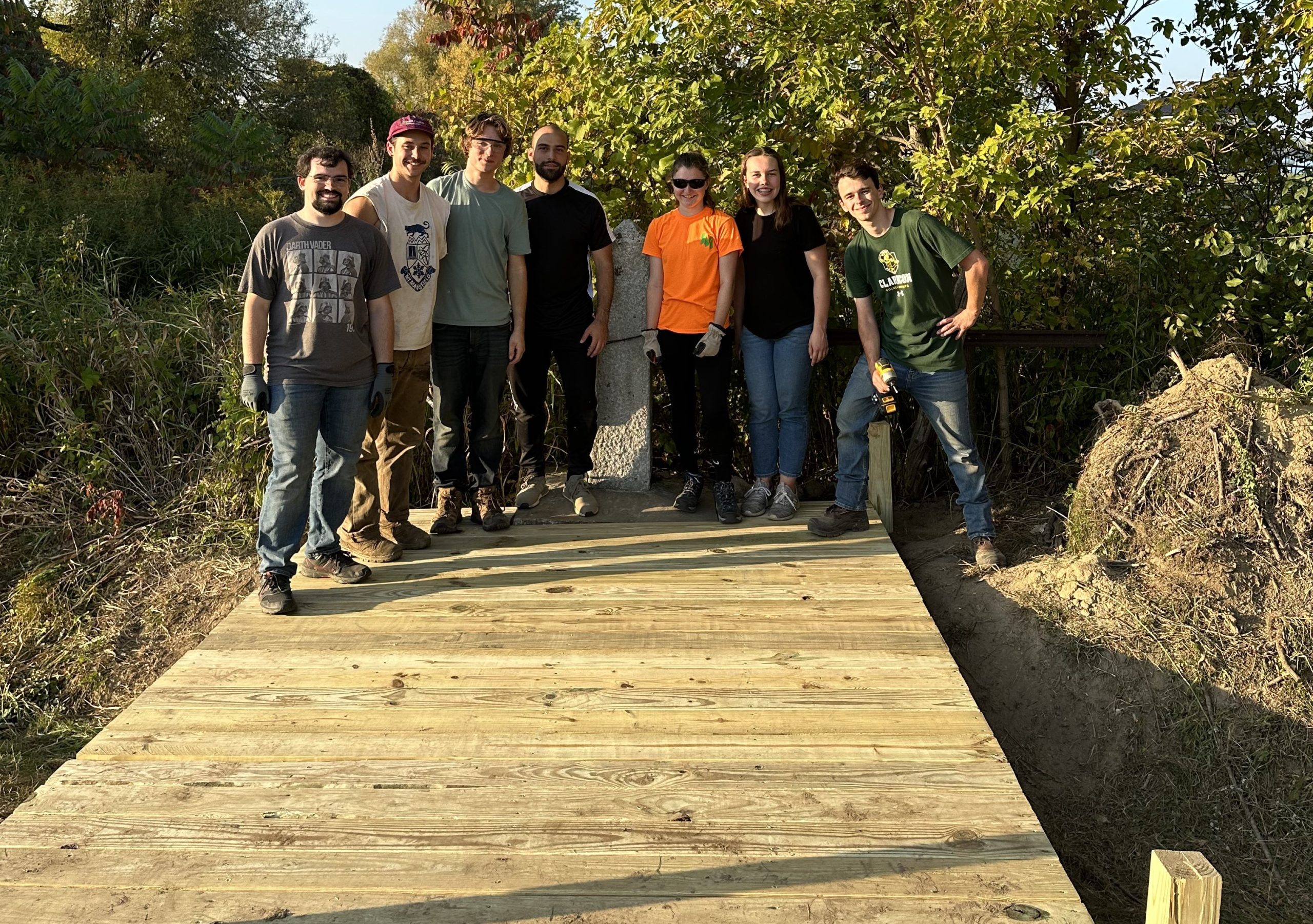 Members of the Timber Bridge SPEED team stand on the bridge they built that leads to a border marker along the US Canada border.