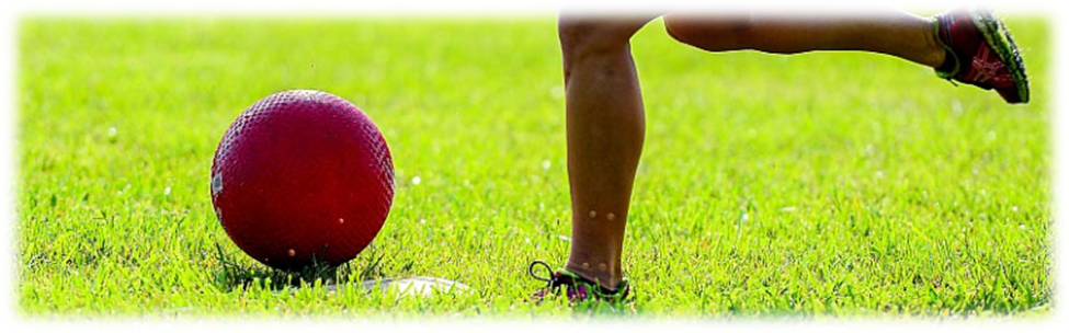 Someone getting ready to kick a red kickball in the grass.