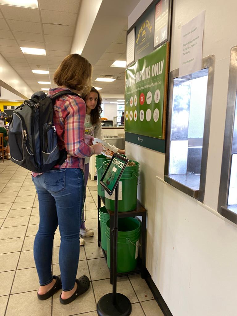 two female students scraping their plates into green food waste buckets at the Ross Brooks dining hall. 