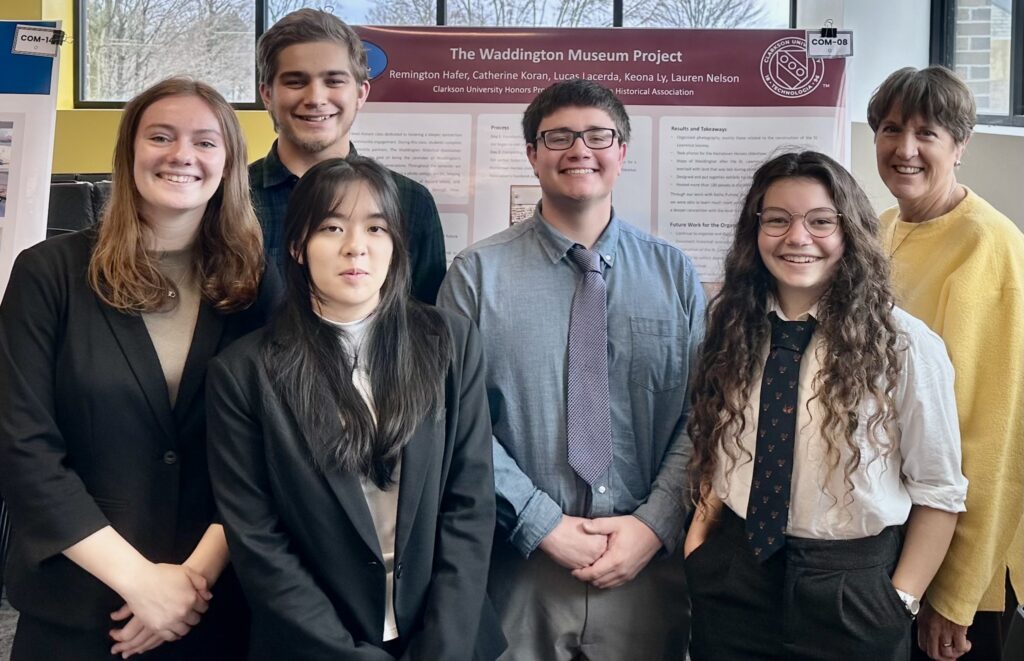 Five students pose for a photo with a local historian in front of a poster explaining the work they did for the Waddington History Museum.