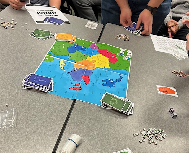 A prototype for a new boardgame made in a Clarkson university class is laid on a table while students prepare to play.